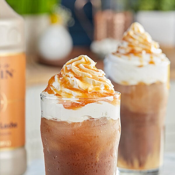 Two drinks with caramel sauce and whipped cream on top.