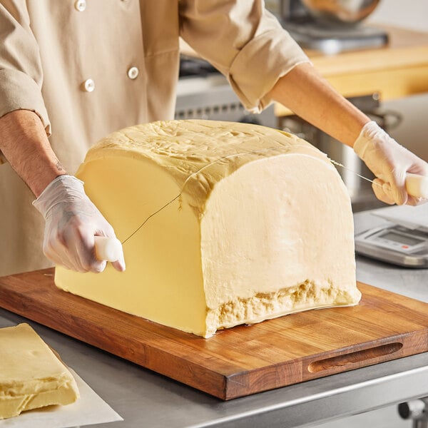 A person cutting a large block of Cabot Grade AA unsalted butter on a counter.