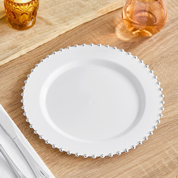 A Visions white plastic plate with silver beaded rim on a table.