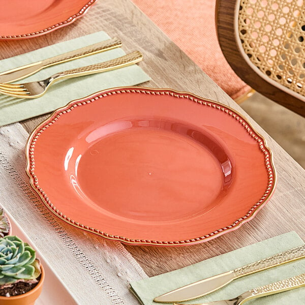 A Visions Terra Cotta plastic plate with a gold vintage rim and utensils on a table.