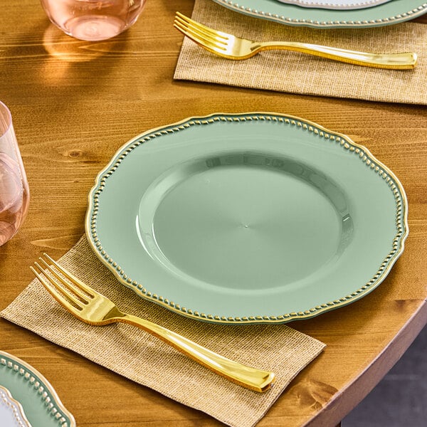 A table set with a Visions eucalyptus round plastic plate with gold vintage rim and a gold fork.