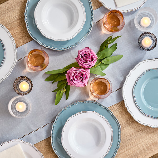 A table set with white Visions plastic bowls with silver vintage rims, plates, and candles.