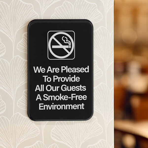A black rectangular sign with white text that reads "We Are Pleased To Provide All Our Guests A Smoke-Free Environment"