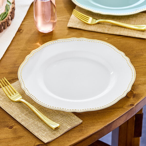 A table setting with Visions white plastic plates with gold vintage rims, forks, and knives.