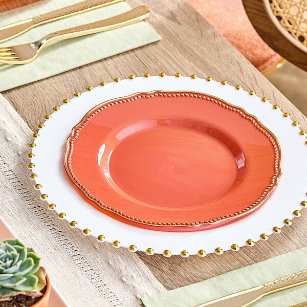 A table setting with a Visions Terra Cotta plastic plate with a gold vintage rim on a table with a knife