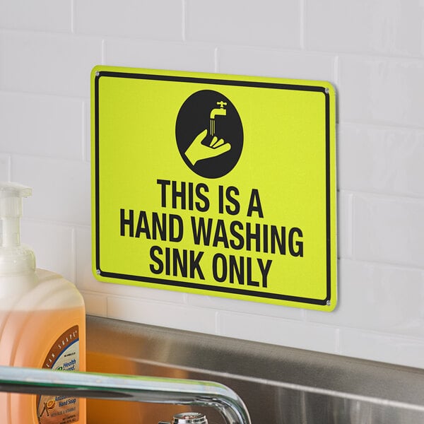 A yellow and black safety sign reading "This Is A Hand Washing Sink Only" on a white tile wall above a sink.