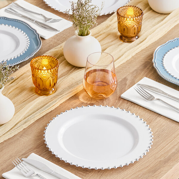 A table set with Visions white plastic plates with silverware and glasses.