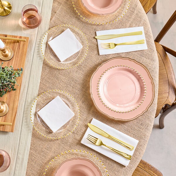 A table set with Visions clear plastic plates with gold beaded rims and gold cutlery.