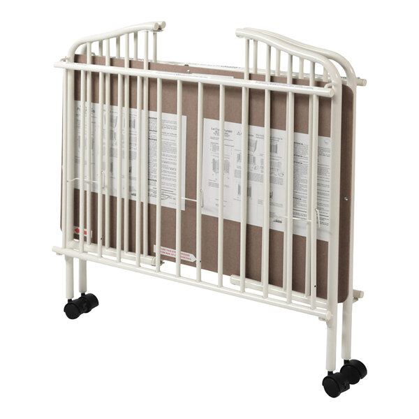 A white metal folding crib with vertical bars and wheels, shown in a folded position with a mattress inside.