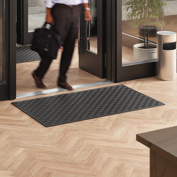 A man walking over a black Lavex Water-Absorbent Parquet Entrance Mat.