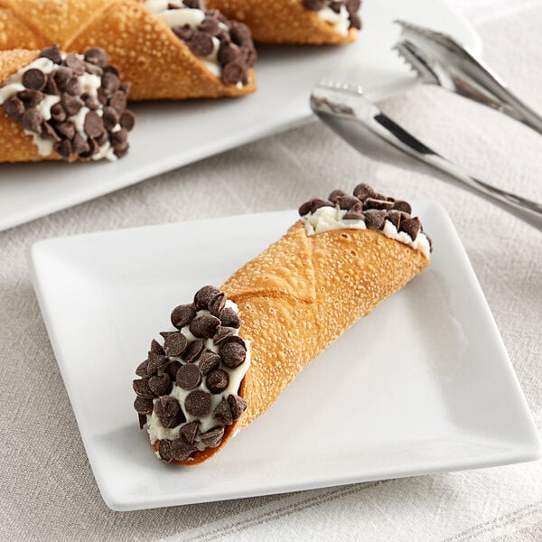 A plate with a Vaccaro's Desserts cannoli with chocolate chips on it and a fork.