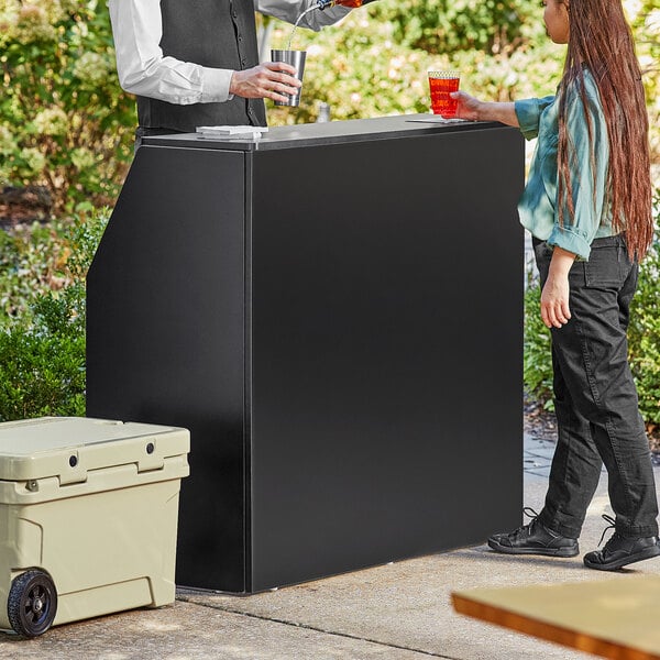 A man and woman standing next to a Lancaster Table and Seating Foldaway Bar on a table in an outdoor catering setup.