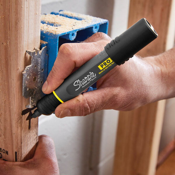 A person using a Sharpie Pro black chisel tip permanent marker to write on a wooden post.