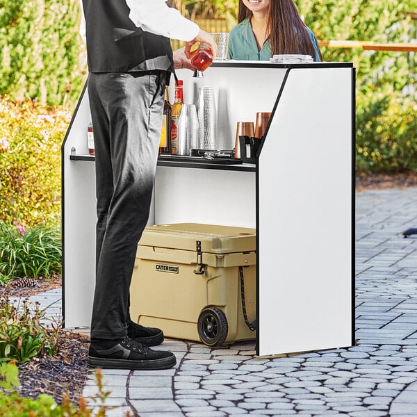 A man and woman standing at a Lancaster Table and Seating foldaway bar with a white laminate finish.
