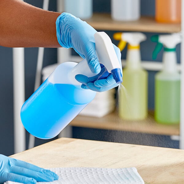 A person in blue gloves using a blue Lavex spray bottle to clean a table.