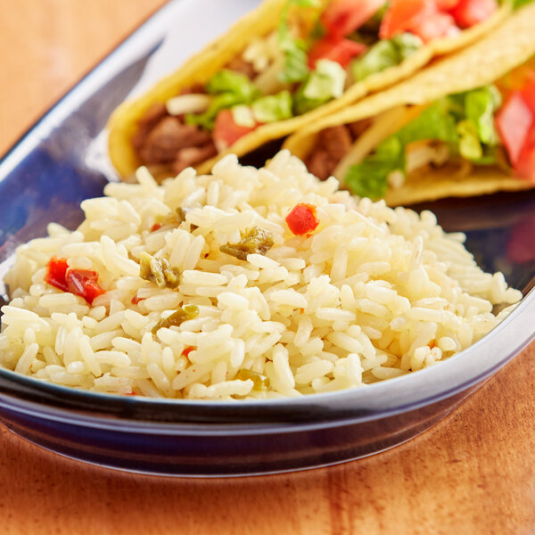 A bowl of Sarita yellow rice on a wooden table with tacos.