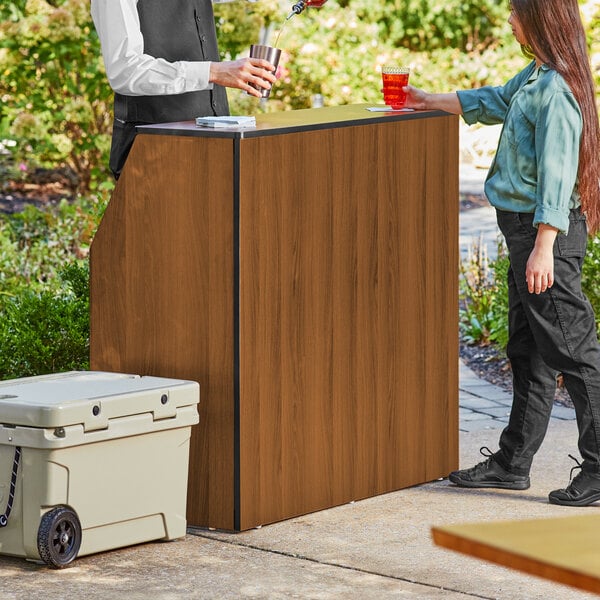 A Lancaster Table and Seating Foldaway Bar with a walnut finish set up outdoors.