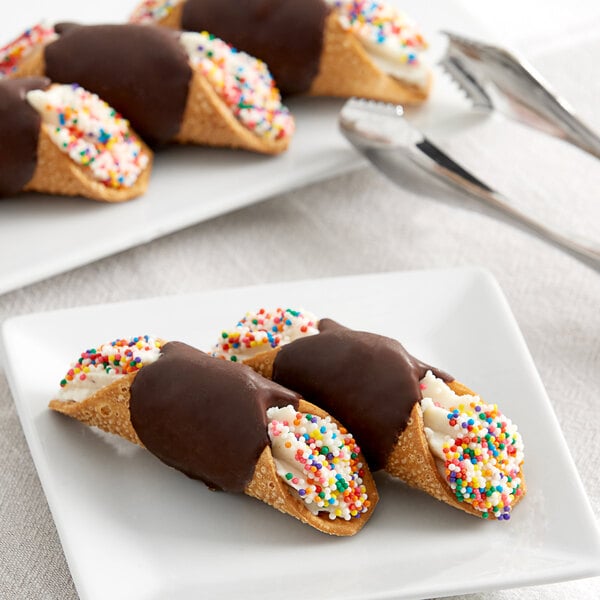 A white plate with two Vaccaro's Mini Chocolate Cannoli shells topped with sprinkles and chocolate.