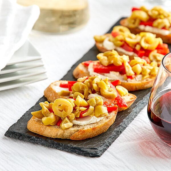A plate of Manzanilla olives with food on a table next to a glass of wine.