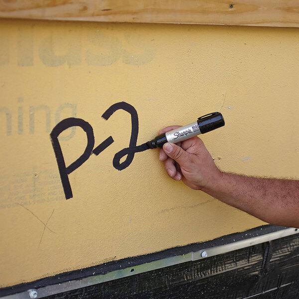 A person using a Sharpie Magnum black chisel tip marker to write on a wall.