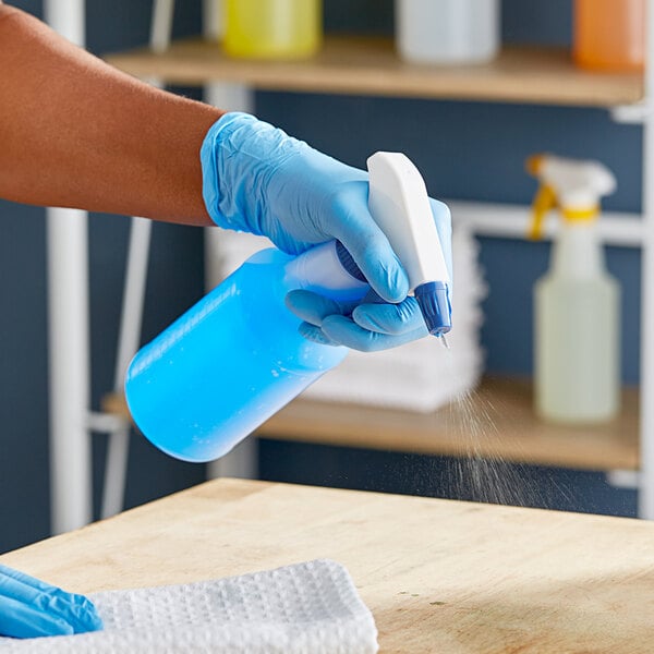 A person in blue gloves using a blue Lavex spray trigger on a bottle.