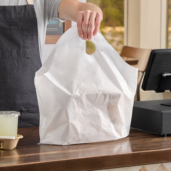 A white unprinted standard-duty plastic wavetop bag with a die-cut handle, being held by a person at a checkout counter.