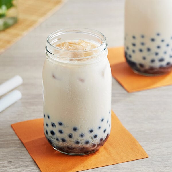 A glass jar filled with white milk tea and black balls on top.