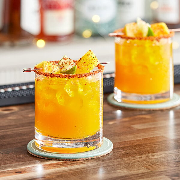 Two glasses of mango drink garnished with limes on a table.