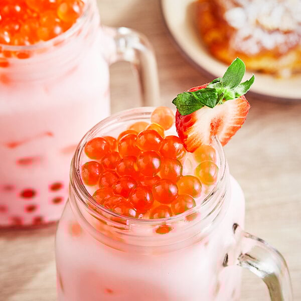 Two glass mason jars filled with pink bubble tea and Possmei Strawberry Popping Boba with a strawberry on top.