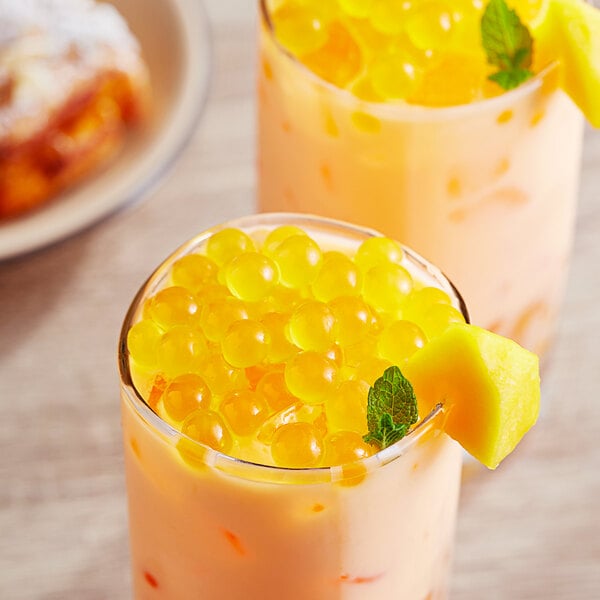 Two glasses of orange mango bubble tea with fruit.