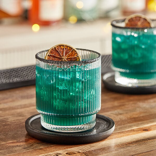 A glass of blue liquid with a slice of orange on a coaster.