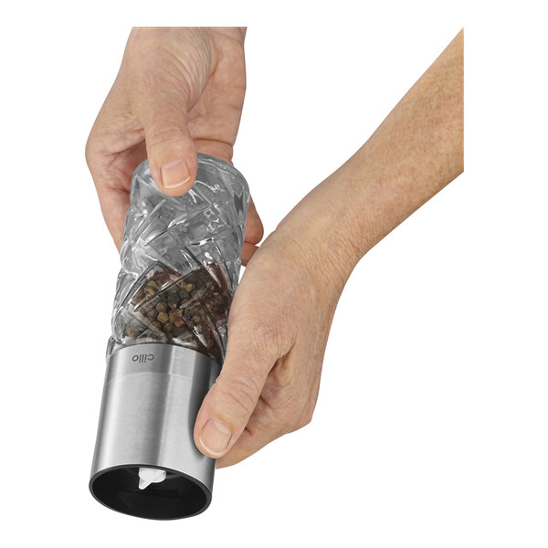 A hand holding a Cilio stainless steel pepper mill.