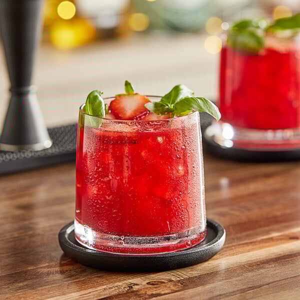 A glass of red strawberry drink with ice, basil, and strawberries.