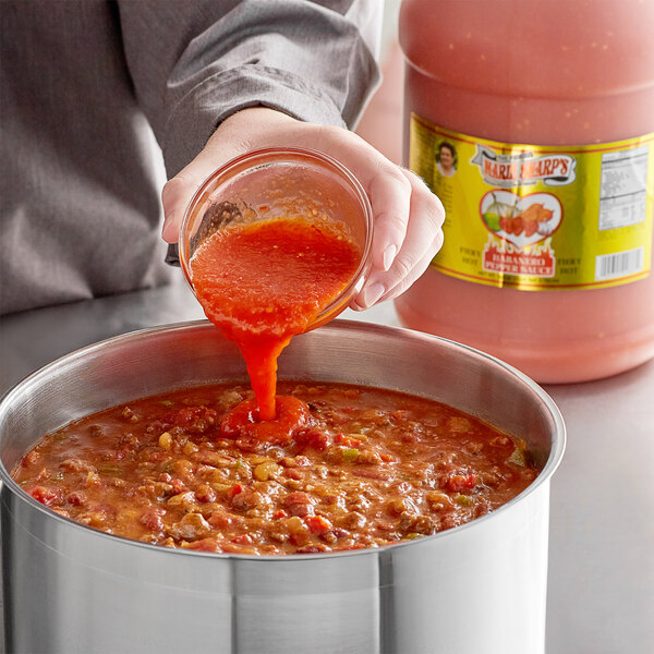 A person pouring Marie Sharp's Fiery Hot Habanero hot sauce into a pot.