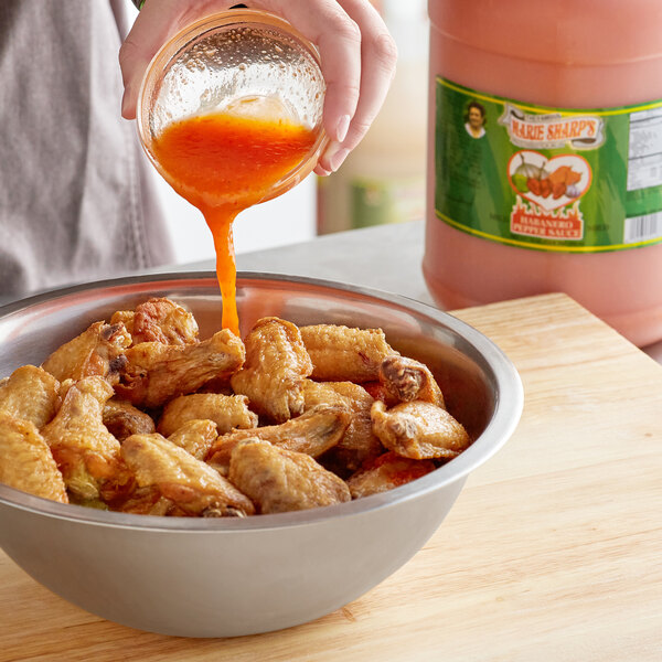A person pouring Marie Sharp's hot sauce into a bowl of chicken wings.