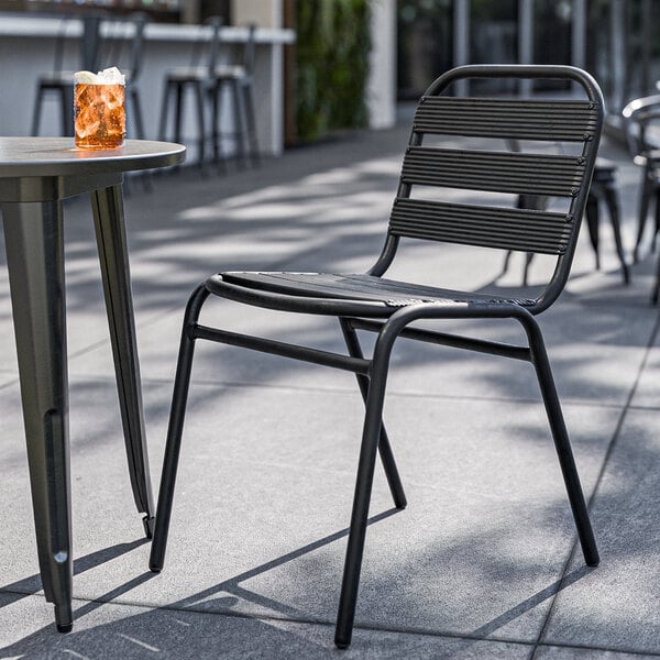 A Lancaster Table & Seating black powder-coated steel outdoor side chair on a patio next to a table with a drink.