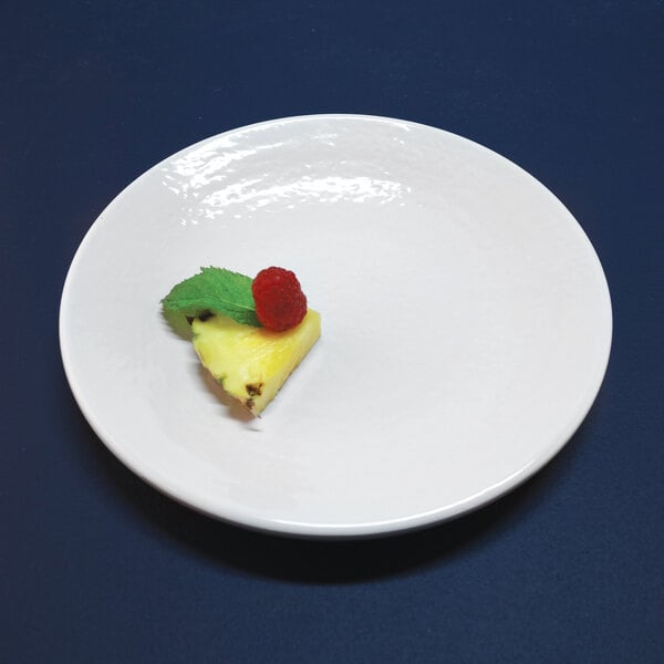 A white Elite Global Solutions round melamine plate with a piece of pineapple with a raspberry on it.