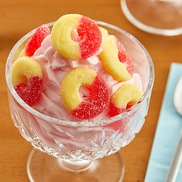 A hand holding a yellow and red Albanese Strawberry Banana Gummi Ring.