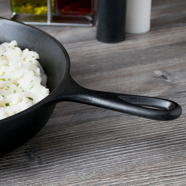 An Elite Global Solutions Illogical Faux Cast Iron fry pan with mashed potatoes and herbs on it.