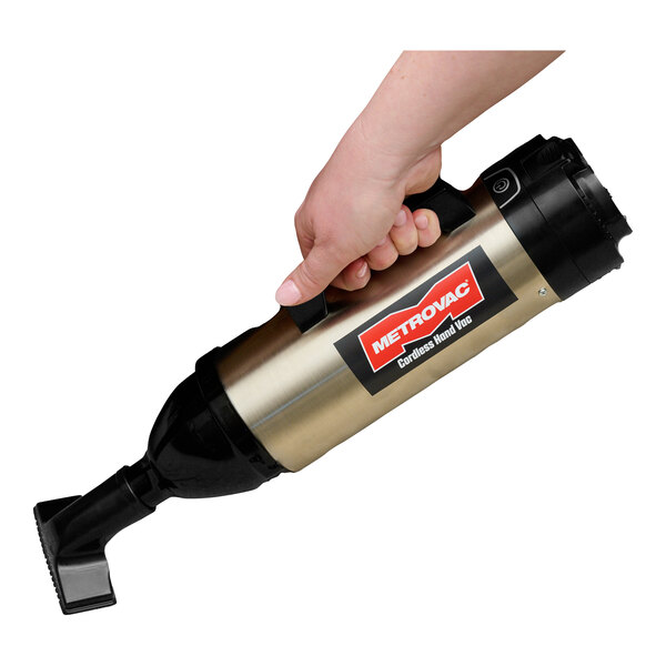 A hand holding a MetroVac cordless handheld vacuum cleaner.