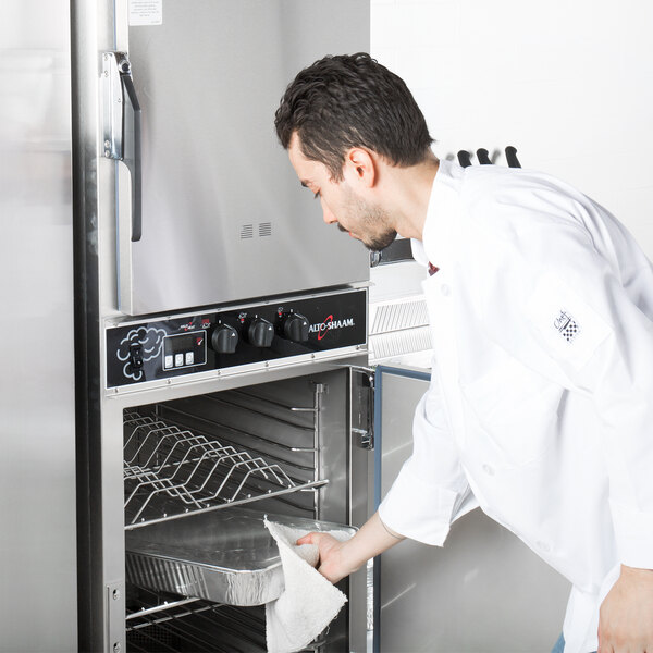 A man in a white coat using an Alto-Shaam smoker oven to cook food.
