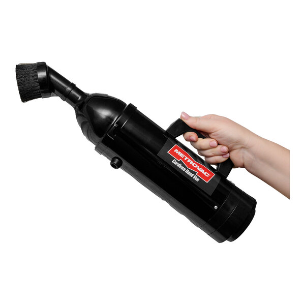 A hand holding a black MetroVac cordless handheld vacuum.