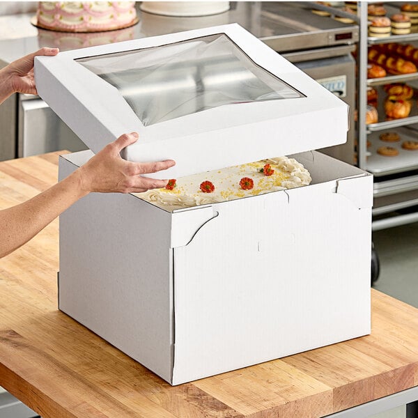 A woman opening a Southern Champion white cake box with a window to reveal a cake inside.