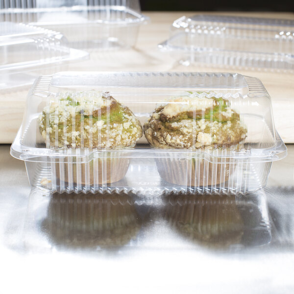 Two muffins in Dart clear plastic take-out containers on a table.