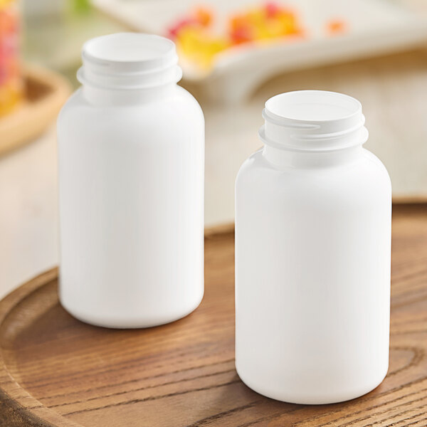 Two white 200cc HDPE packer bottles with white lids on a wooden surface.