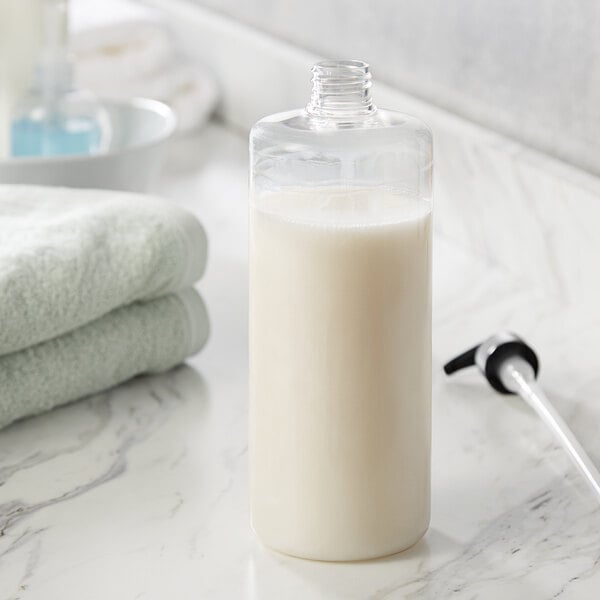A 32 oz. clear PET cylinder bottle on a counter full of liquid.