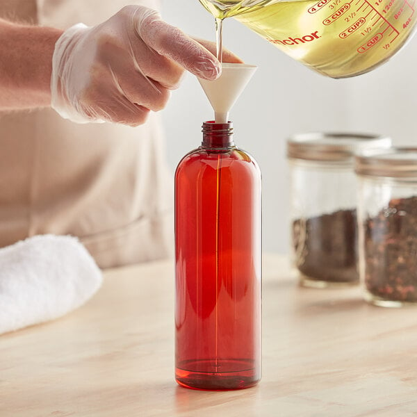 A person pouring liquid into a Boston Round PET amber bottle.