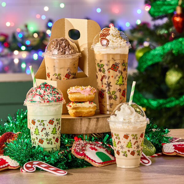 A set of clear 16 oz. plastic cold cups decorated with holiday-themed prints, filled with festive drinks and surrounded by Christmas decorations.