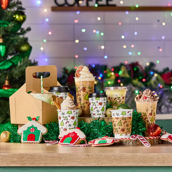 A group of festive holiday-themed cold cups filled with various drinks, surrounded by Christmas decorations and cookies.