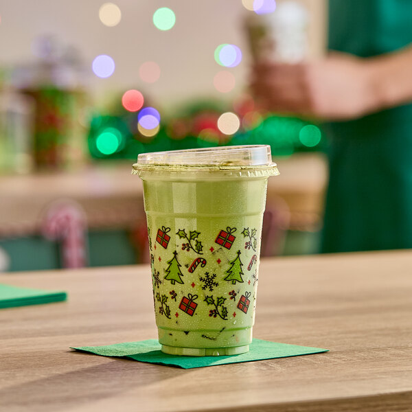 A 16 oz. clear plastic cold cup with holiday-themed decorations, filled with a green beverage and topped with a plastic lid.